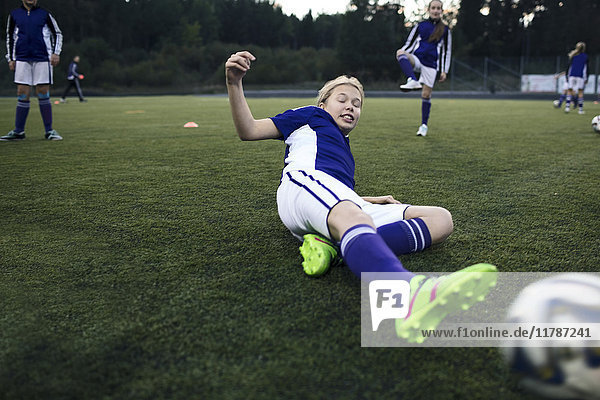 Mädchen rutscht während des Trainings auf Rasen auf dem Fußballfeld
