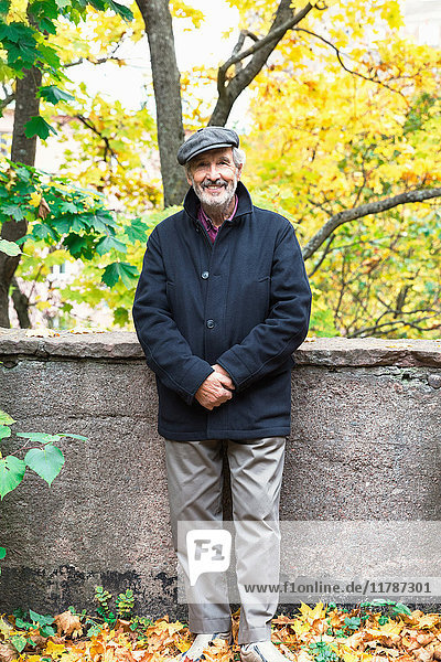 Porträt eines glücklichen älteren Mannes  der im Herbst mit den Händen im Park steht.