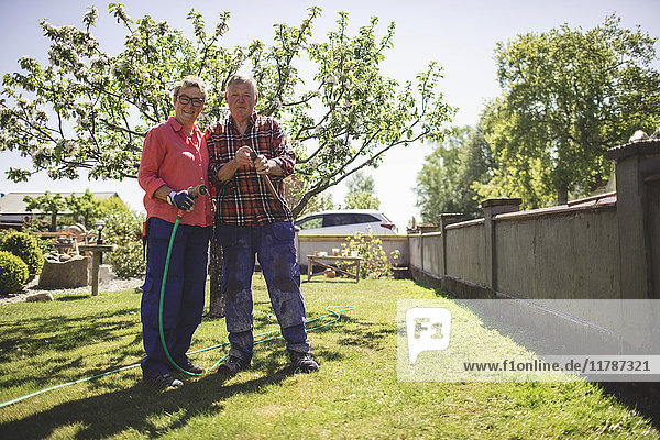 Ganzkörperporträt eines älteren Paares mit Hammer und Gartenschlauch im Hof stehend
