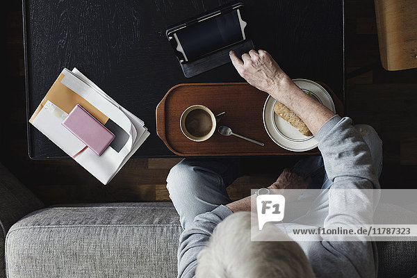 Direkt über der Aufnahme eines älteren Mannes mit digitalem Tablett beim Frühstück zu Hause.