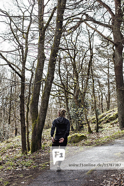 Full length rear view of female athlete doing stretching exercise on road in forest