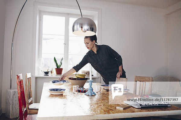 Junge Frau arrangiert Teller auf dem Esstisch zu Hause
