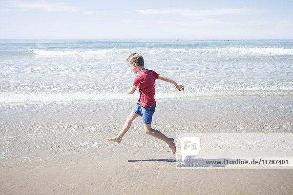 Durchgehende Seitenansicht des Jungen  der an einem sonnigen Tag am Strand läuft.