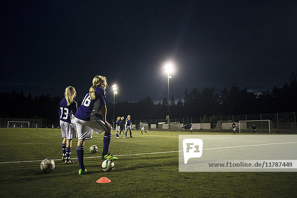 Mädchen üben Fußball auf dem Spielfeld gegen den Himmel bei Nacht