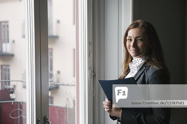 Porträt einer selbstbewussten  reifen Immobilienmaklerin mit Schaufensterprospekt zu Hause
