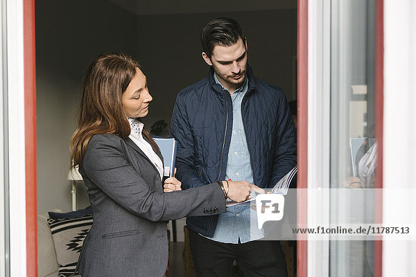 Female realtor assisting man while pointing at brochure by window