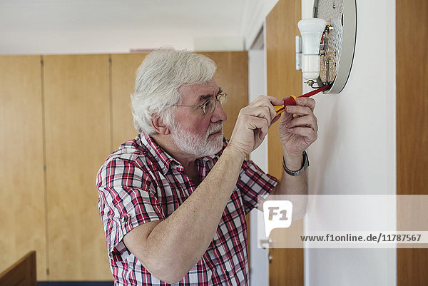Senior Mann repariert Wandleuchter mit Schraubendreher zu Hause