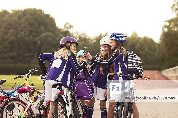 Mädchen zeigen Freunden  die mit Fahrrädern auf dem Fußweg gegen den Himmel stehen  ihr Handy.