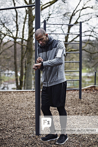 Full length of male athlete checking smart watch while leaning on pole in forest