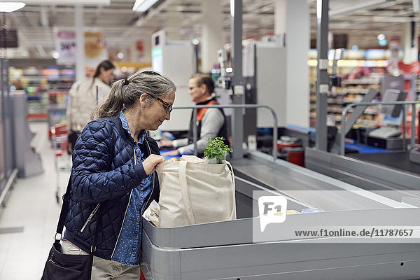 Smiling mature woman holding bag at checkout counter in supermarket