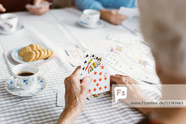 Abgeschnittenes Bild einer älteren Frau  die mit ihrer Familie am Tisch Karten spielt.