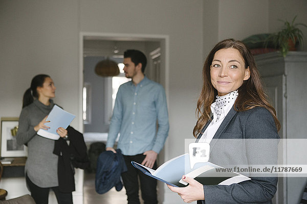 Confident female realtor holding brochure while couple standing in background