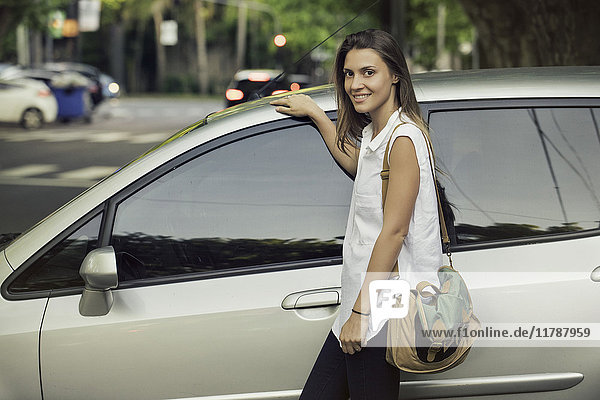 Young woman leaning against car  smiling