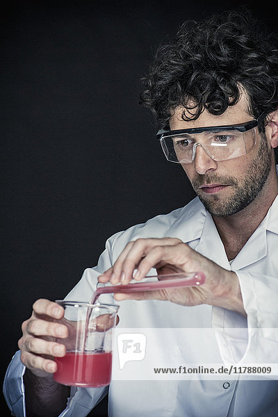 Chemiker gießt Flüssigkeit aus dem Reagenzglas in das Becherglas