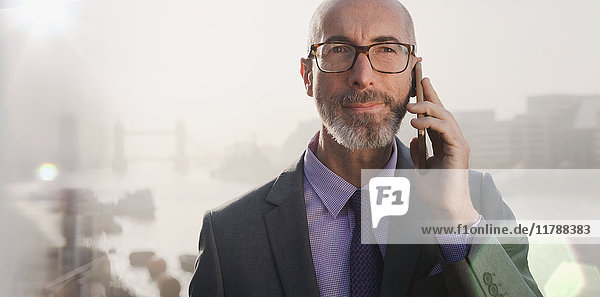 Portrait serious businessman talking on cell phone on urban bridge  London  UK