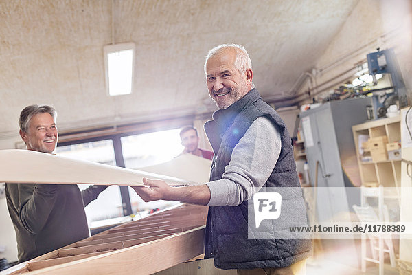 Portrait lächelnder älterer Schreiner beim Heben von Holzbooten in der Werkstatt