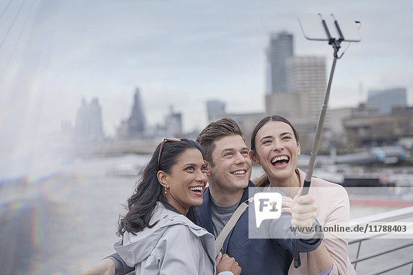 Enthusiastic  smiling friend tourists taking selfie with selfie stick on urban bridge  London  UK