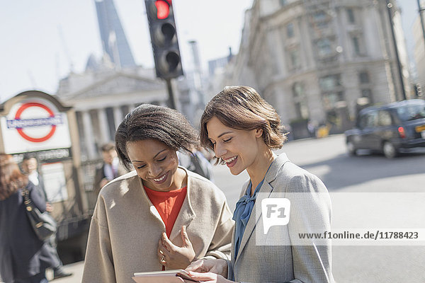 Lächelnde Geschäftsfrauen mit digitalem Tablett im Gespräch auf der sonnigen Stadtstraße