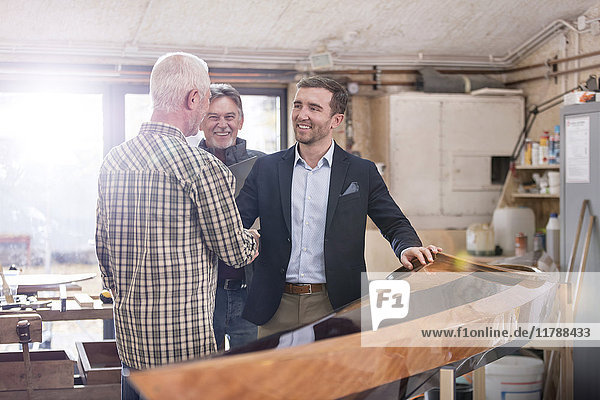 Male carpenters handshaking with satisfied customer next to wood kayak in workshop