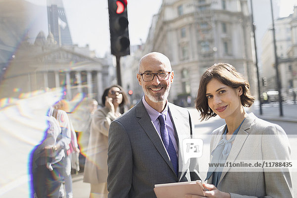 Portrait lächelnde  selbstbewusste Geschäftsleute mit digitalem Tablett auf der sonnigen City Street  London  UK