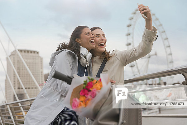 Enthusiastische  lächelnde Frauenfreunde  die Selfie mit Fotohandy in der Nähe von Millennium Wheel  London  UK nehmen