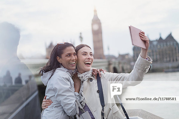 Enthusiastische  lächelnde Freundinnen  die sich mit einer digitalen Tablettkamera in der Nähe von Big Ben  London  UK  vergnügen.