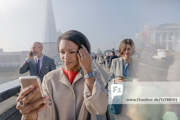 Geschäftsfrau mit Handy auf der sonnigen städtischen Fußgängerbrücke London UK