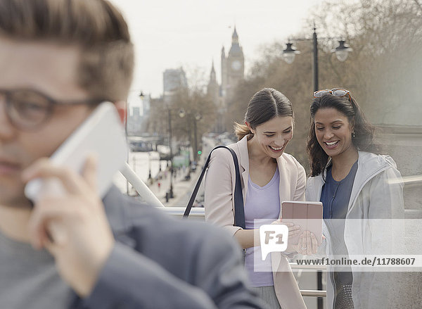 Female friends using digital tablet on urban bridge  London  UK