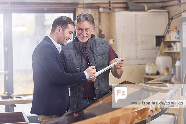 Männliche Kunden unterschreiben Papierkram für fertiges Holzkajak in der Werkstatt