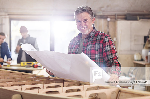 Portrait lächelnder Schreiner bei der Begutachtung von Plänen am Holzboot in der Werkstatt