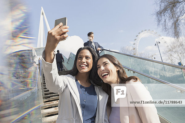 Enthusiastic  smiling women friends taking selfie with camera phone on sunny  urban stairs  London  UK