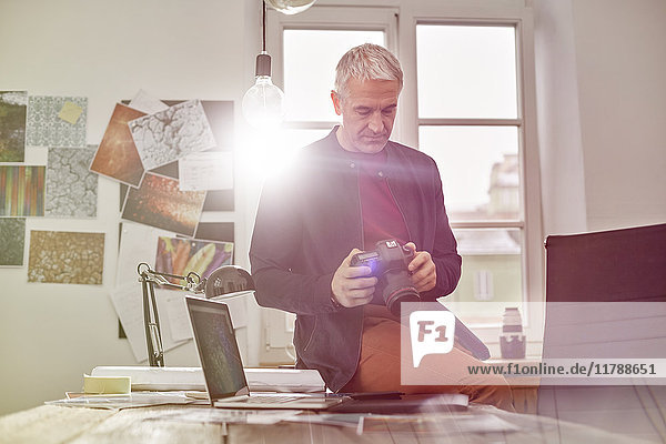 Male photographer using digital camera in sunny office