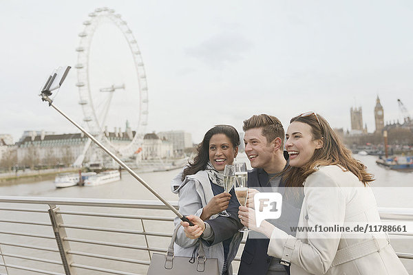 Smiling friend tourists celebrating  toasting champagne and taking selfie with selfie stick near Millennium Wheel  London  UK