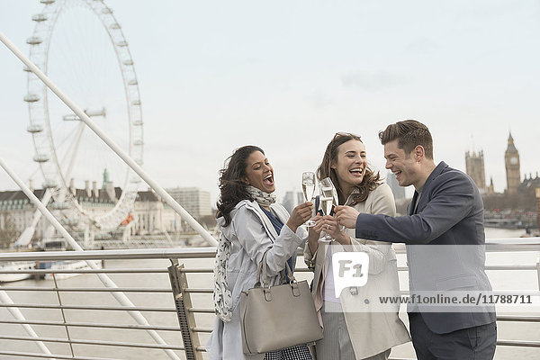 Enthusiastic  smiling friends celebrating  toasting champagne on urban bridge near Millennium Wheel  London  UK