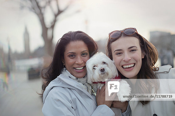 Portrait smiling lesbian couple with white dog in urban park