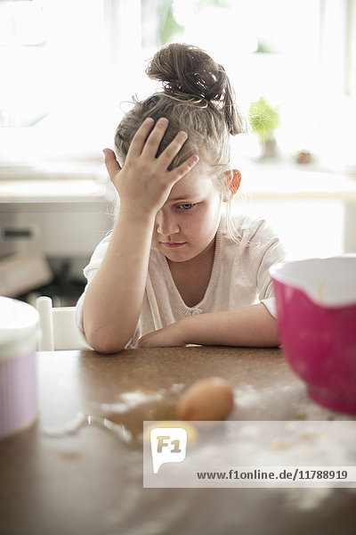Kleines Mädchen beobachtet zerbrochenes Ei auf dem Küchentisch