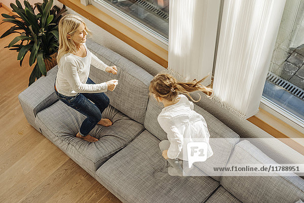 Reife Frau und Mädchen zu Hause auf der Couch hüpfend