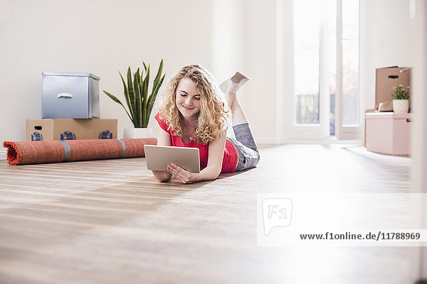 Young woman in new home lying on floor with tablet