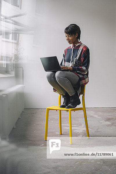 Junge Frau sitzt auf Stuhl mit Laptop