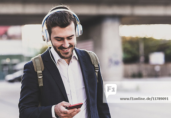 Smiling young man owearing headphones checking cell phone