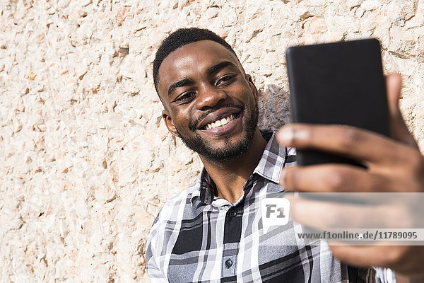 Porträt eines lächelnden jungen Mannes  der sich selbst mit dem Handy fotografiert.