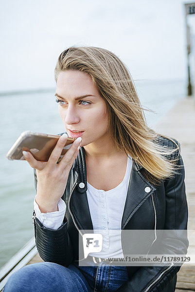 Junge Frau am Telefon sitzend auf der Promenade