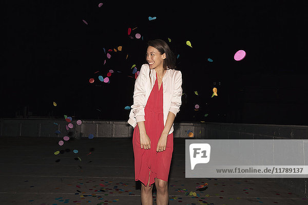 Young woman standing on a rooftop terrace with flying confetti