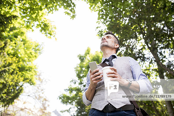 Geschäftsmann mit Kaffee und Smartphone im Stadtpark