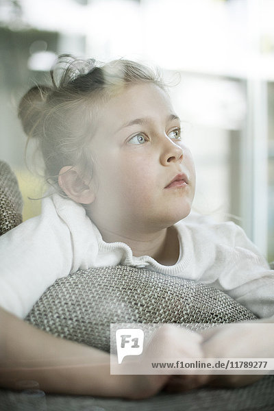 Porträt eines ernsthaften kleinen Mädchens  das aus dem Fenster schaut.