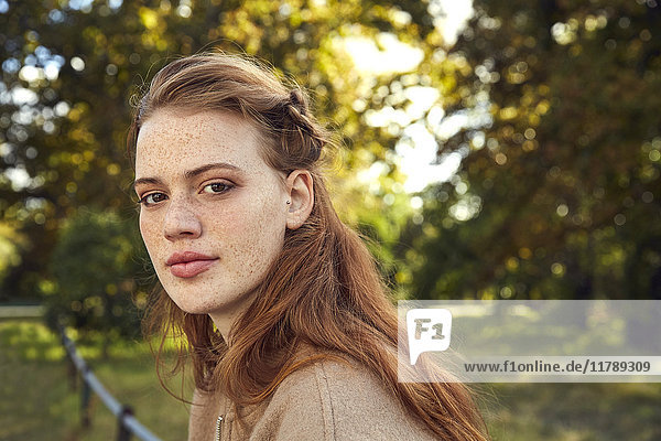 Portrait of redheaded young woman with freckles in a park