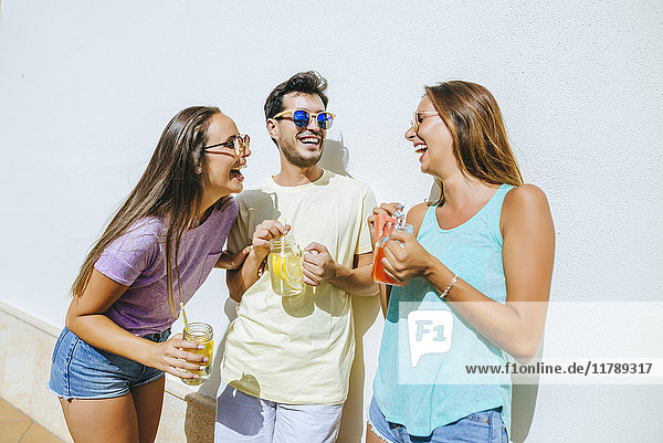 Lachende Freunde mit erfrischenden Getränken vor der weißen Wand