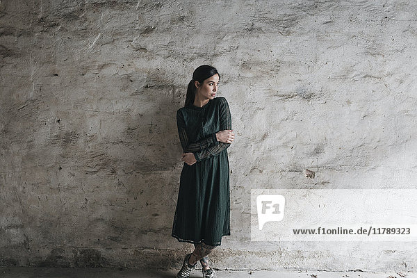 Junge Frau in grünem Kleid  vor der Wand stehend