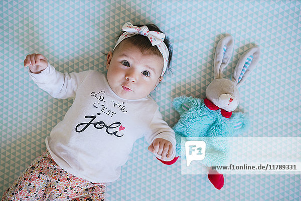Baby girl lying on bed beside toy bunny