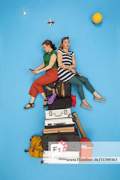 Friends sitting on pile of luggage waiting for departure  looking bored